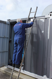 A painter painting a large container while working from a set of ladders